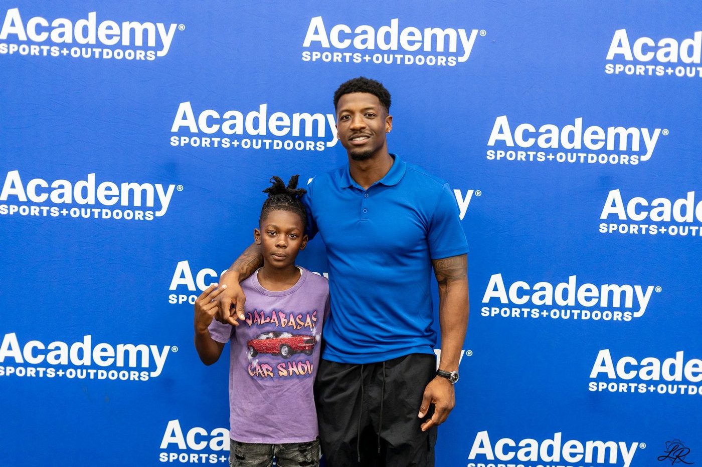 Anthony Miller II posing with a young girl at the Academy Sports backdrop